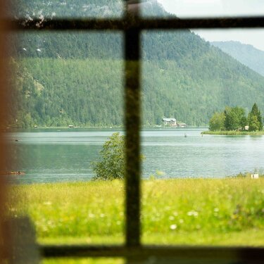View of a serene lake framed by window panes, surrounded by lush green mountains and trees.