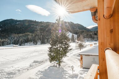 Winter landscape with snow-covered trees and a sunbeam, viewed from a wooden balcony.