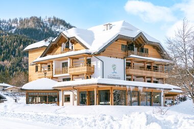 A wooden alpine-style building surrounded by snow and mountains, featuring a sign that says 'Leonhard'.