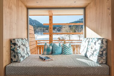 Cozy reading nook with cushions and a view of snowy mountains through a large window.