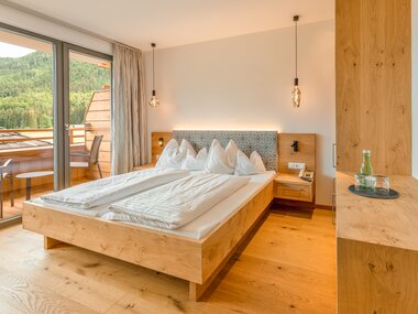 Helles, modernes Schlafzimmer mit Doppelbett, Holzmöbel und Zugang zu einem Balkon mit Blick auf die Natur.
