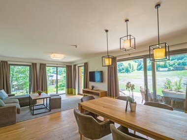 Moderne, helle Wohn- und Esszimmer mit Holzdetails und großen Fenstern zur Natur.