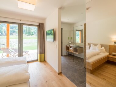Helles, modernes Hotelzimmer mit Blick auf einen Garten, Bad und Holzinterieur.