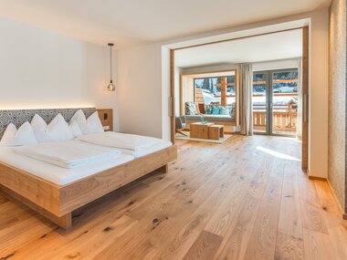 Ein geräumiges Hotelzimmer mit einem Doppelbett, weißen Bettdecken, Holzakzenten und großen Fenstern mit Blick auf eine verschneite Landschaft.