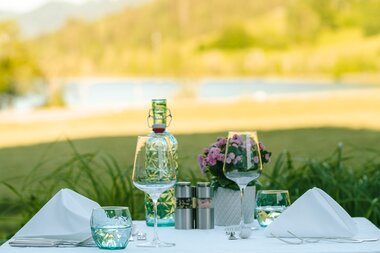 An elegantly set outdoor dining table with glasses, a water bottle, and a flower arrangement, overlooking a scenic landscape.