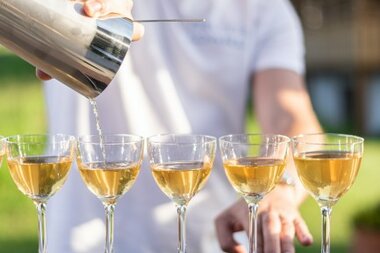 Ein Barkeeper gießen einen Cocktail aus einem Shaker in fünf elegante Gläser an einer Bar.