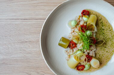 Ein kunstvoll angerichtetes Gericht mit Getreide, Lauch, getrockneten Tomaten und grüner Sauce.