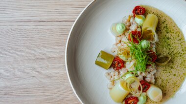 An artfully plated dish featuring grains, leeks, sun-dried tomatoes, and green sauce.