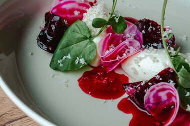 Ein Gourmetgericht mit leuchtenden Rüben, Sahne und Kräutern, kunstvoll auf einem Teller angerichtet.