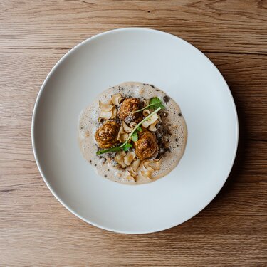 A gourmet dish featuring three roasted spheres on a circular plate, garnished with herbs and slices of vegetable.