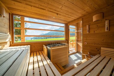 Interior of a modern sauna with wooden benches and a scenic view through large windows.