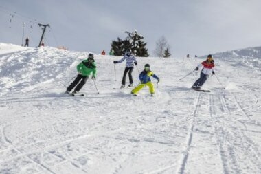 Four skiers in colorful gear skiing down a snowy slope.