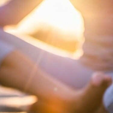 Eine Person meditiert in der Yoga-Haltung, im Schneidersitz auf einer Matte in einem Feld während des Sonnenuntergangs.