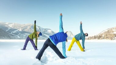 Three people stretching in the snow against a mountain landscape.